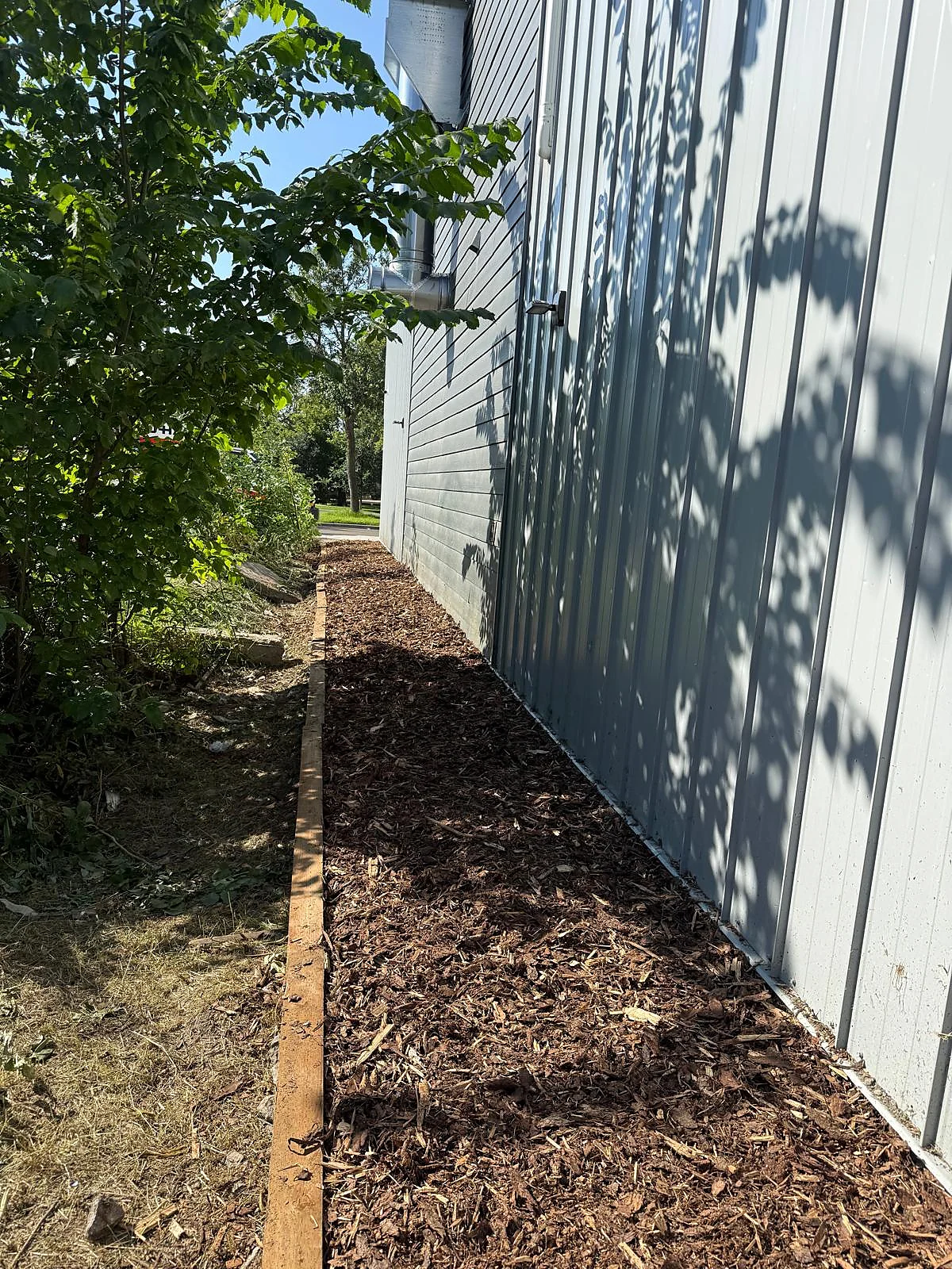 Completed mulch bed beside a building and timber edging